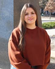 A photo of Emily in a burnt orange sweater, outside. 
